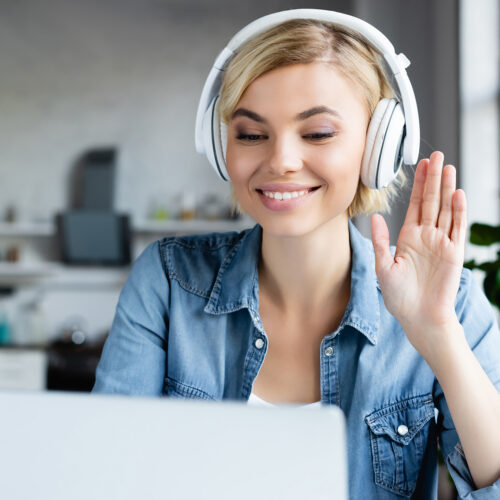 young blonde woman in headphones having online conference and waving hand