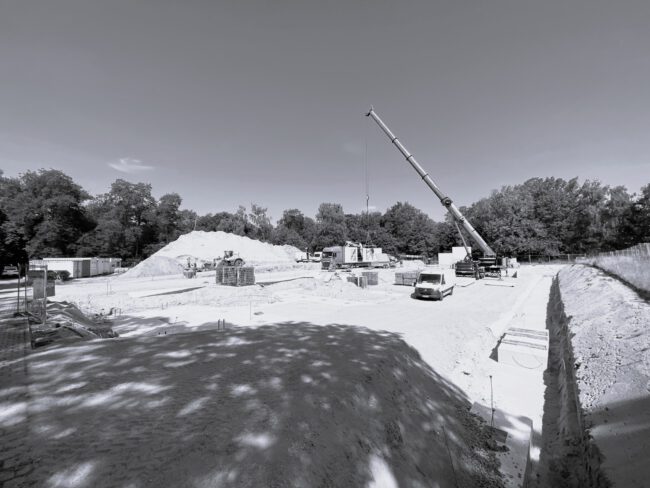 Baustelle Berlin_sw Schwarz-Weißbild von einer Baustelle, mit einem Kran und einem Auto. Die Fläche ist noch ohne Beton, mit Schotter aufgefüllt.